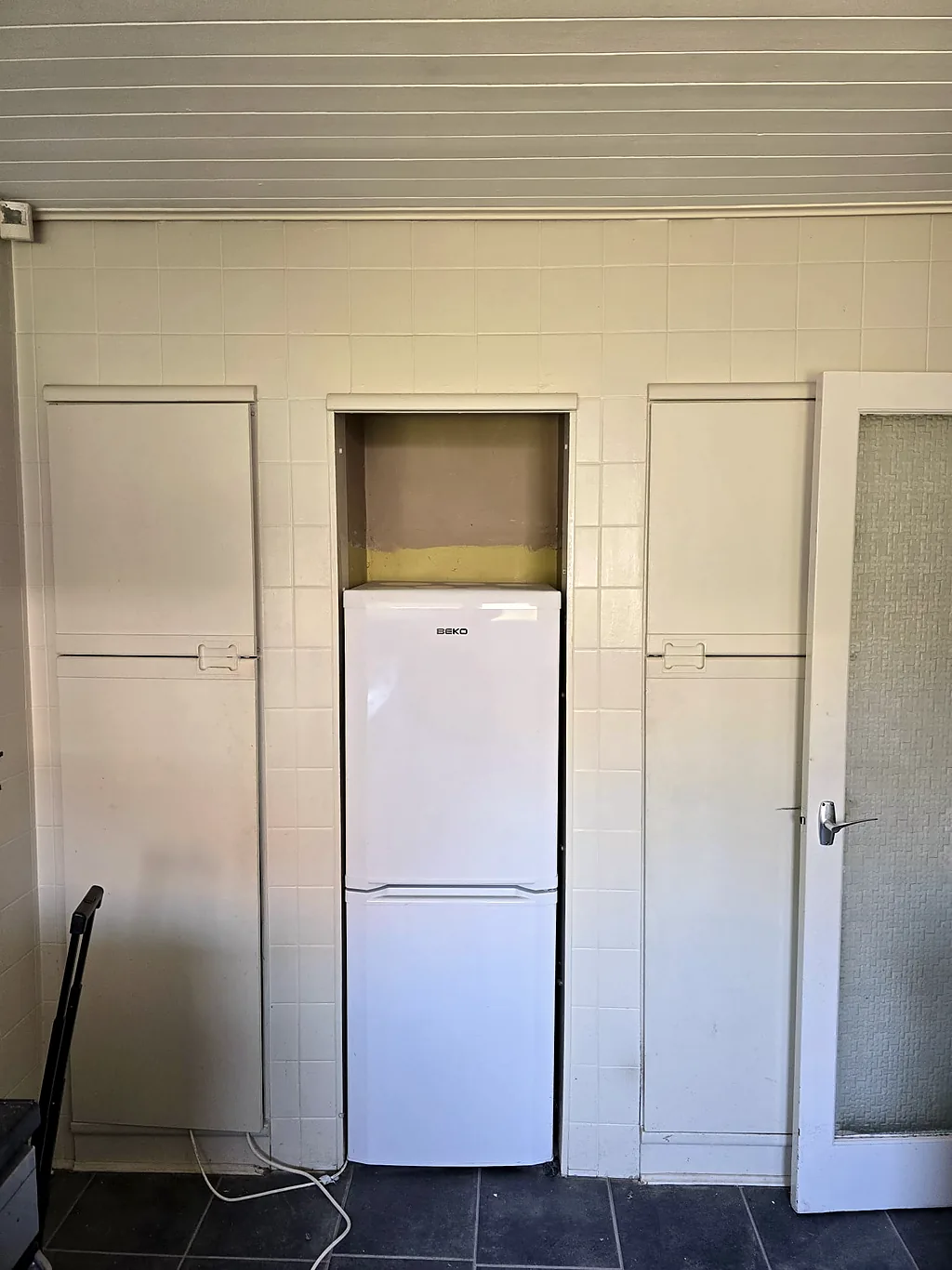 Dated kitchen with a freestanding fridge in a tiled alcove before the refit