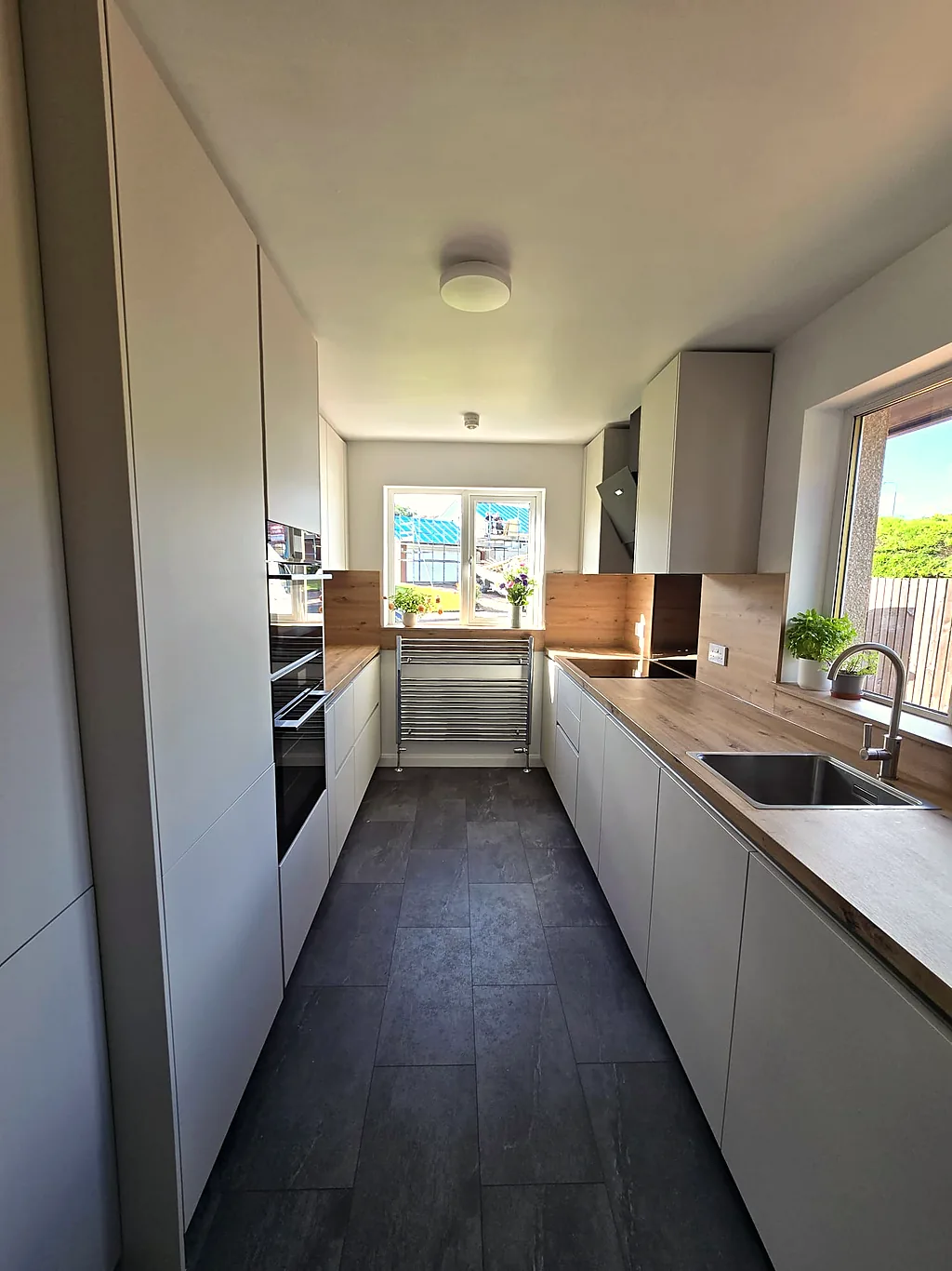 White handleless galley kitchen with wood-effect worktops after renovation