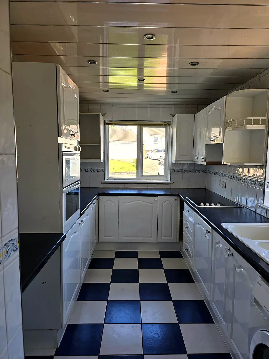 Dated white kitchen with a navy-and-white checkerboard floor before the refit